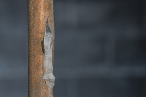 A close-up of a frozen copper pipe covered in frost against a basement wall. Burst pipe causing water damage.