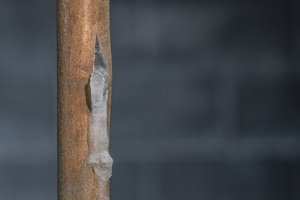 A close-up of a frozen copper pipe covered in frost against a basement wall. Burst pipe causing water damage.